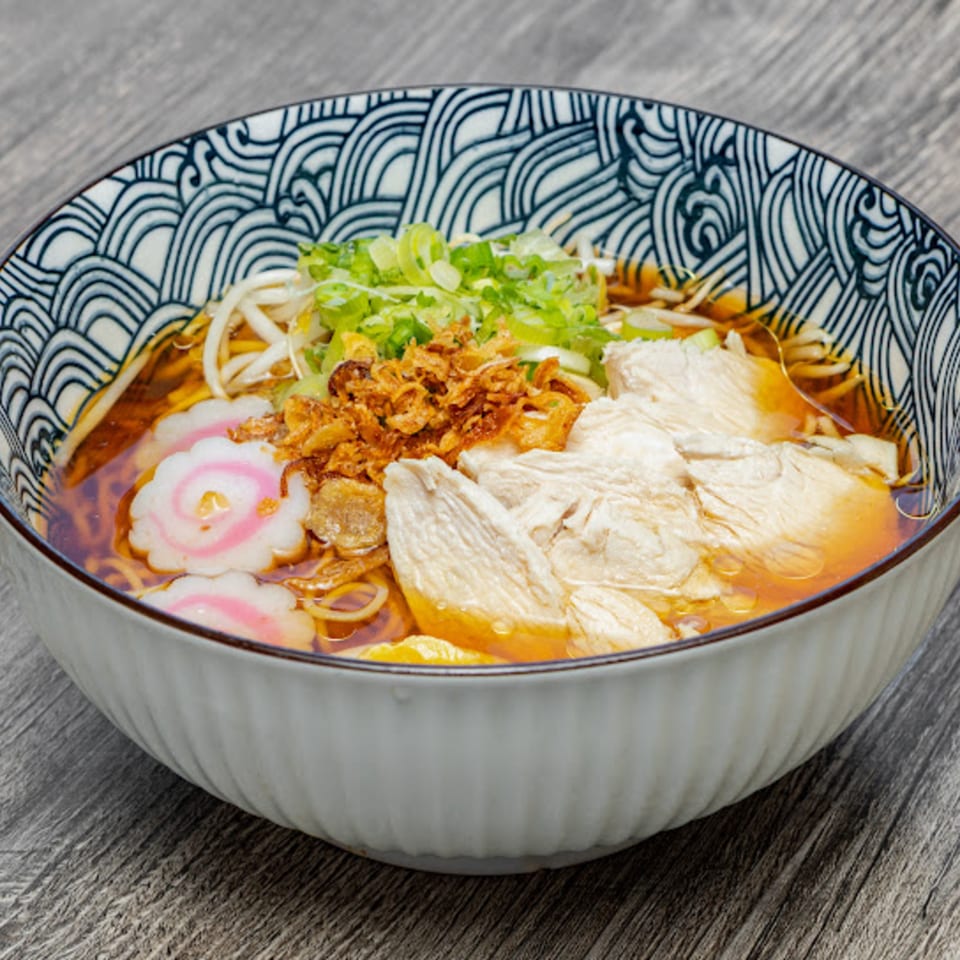 Motto Ramen's chicken ramen with fish cakes, scallions, and fried onions in a decorative bowl.