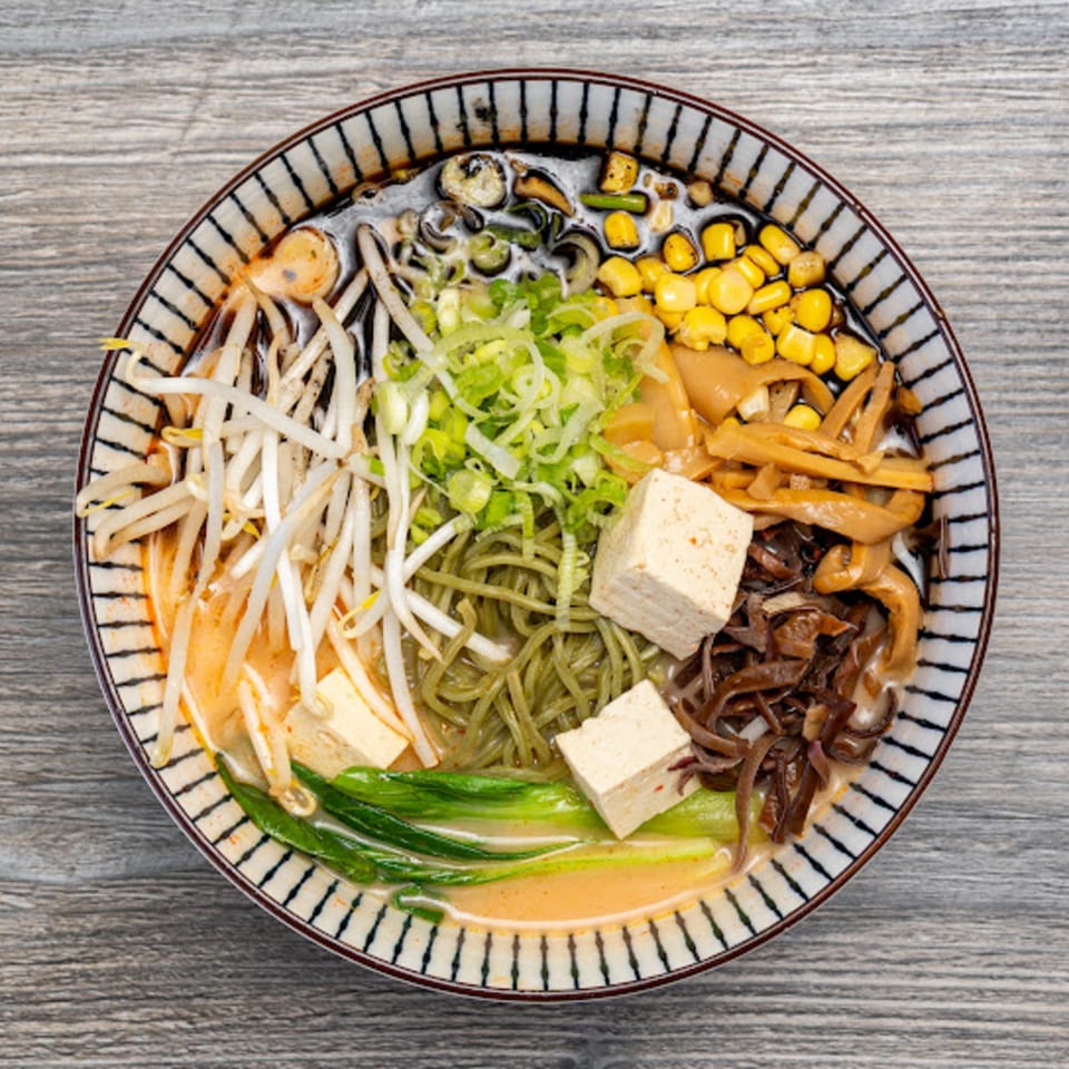 Overhead view of a colorful bowl of Motto Ramen with tofu, corn, green onions, and bean sprouts.