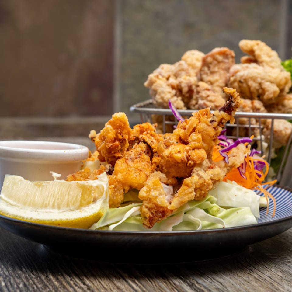 Crispy fried calamari with lemon, dipping sauce, and shredded vegetables on a plate.