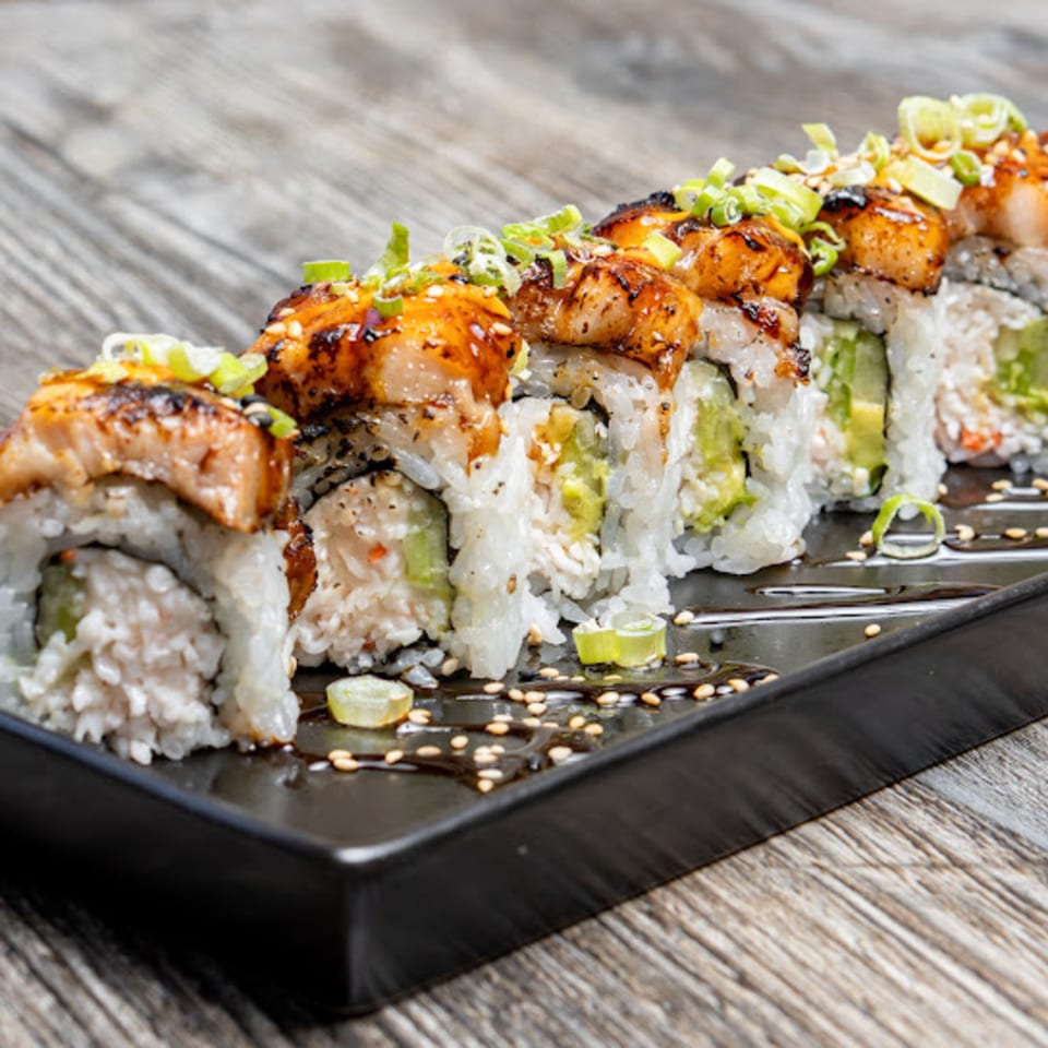 Motto Ramen's sushi roll with seared fish, avocado, and green onions on a black plate.