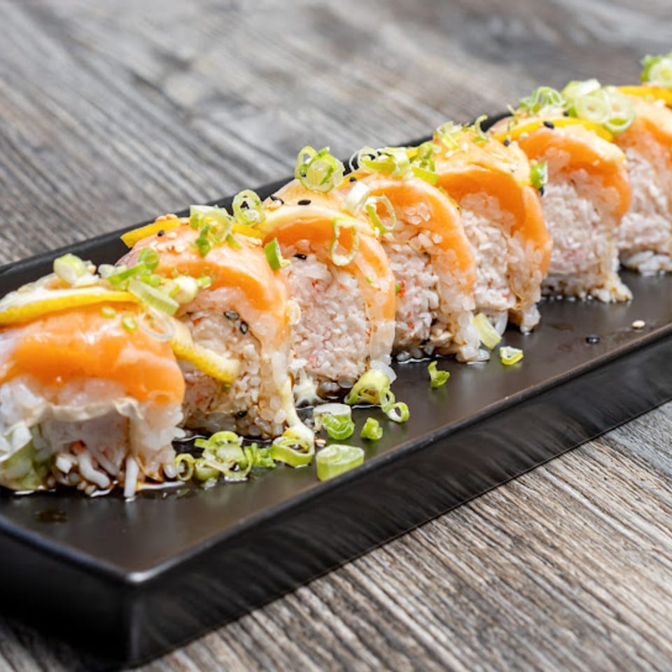 Motto Ramen's sushi rolls with salmon, lemon, and green onions on a black plate.