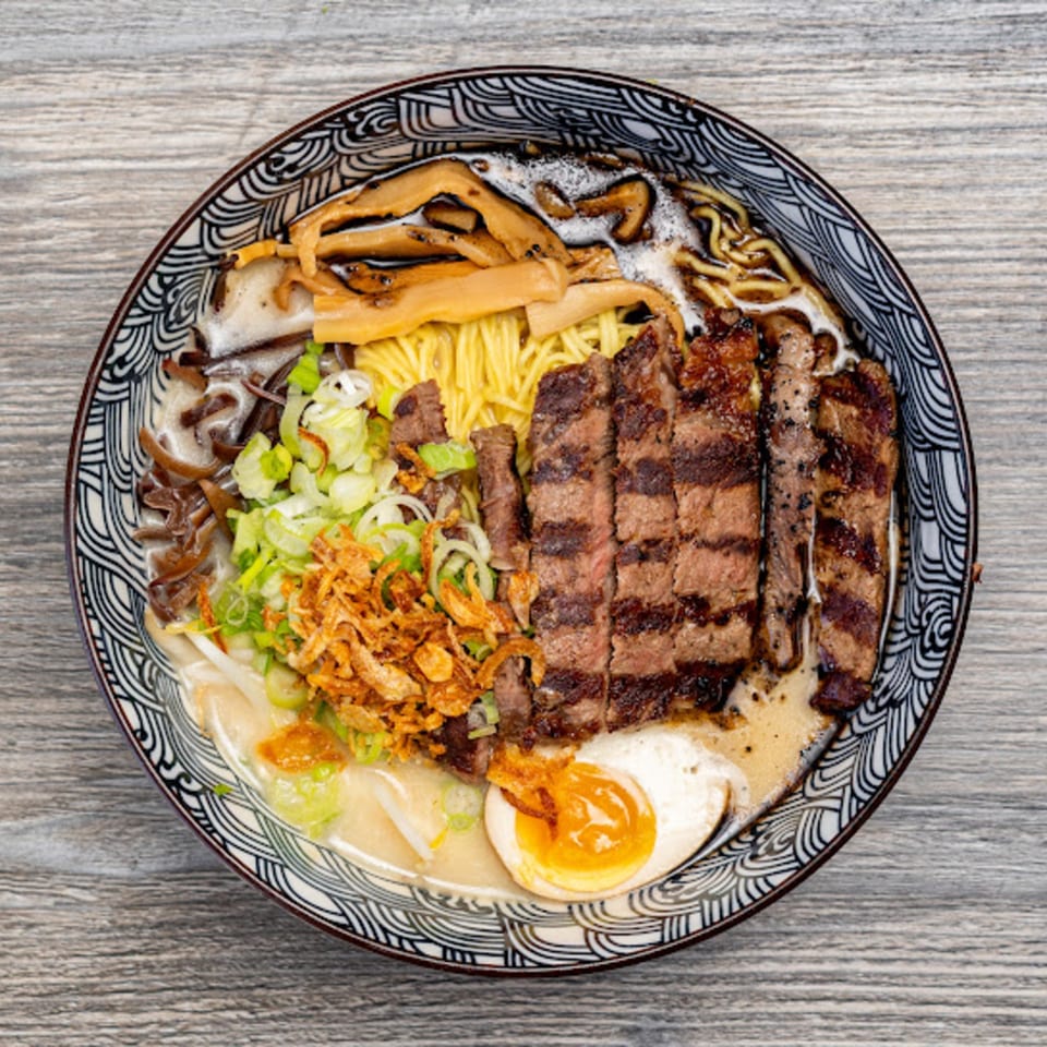 Overhead view of Motto Ramen's ramen bowl with sliced steak, noodles, egg, and vegetables.